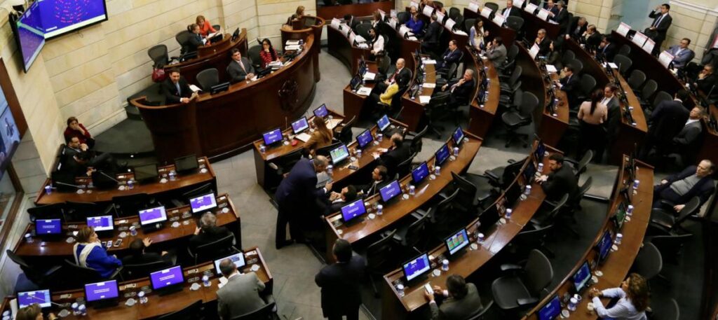 Punto de vista aéreo del Capitolio Nacional de Colombia, mostrando una sesión plenaria del Congreso con senadores y representantes debatiendo.