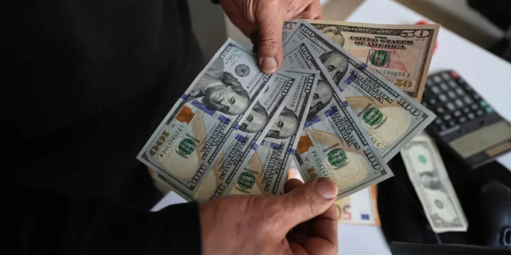 Persona contando billetes de dólares americanos sobre un escritorio con calculadora para calcular el precio del dólar en Colombia.