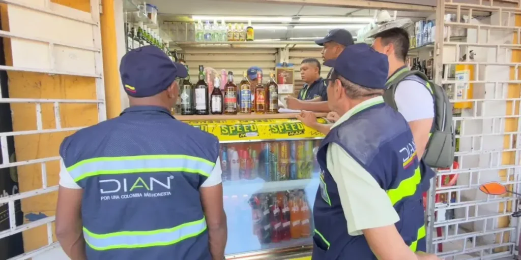 Funcionarios de la DIAN con chalecos oficiales realizando una inspección en una tienda o cigarrería local.