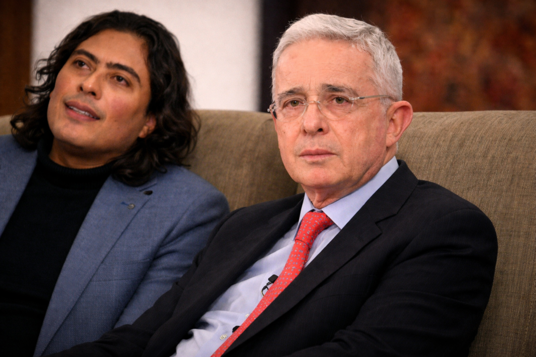 Una imagen compuesta lado a lado que muestra a Álvaro Uribe Vélez (izquierda) y Nicolás Petro Burgos (derecha). Uribe está serio y de traje, idéntico a image_14.png, mientras Nicolás Petro, también de blazer, está pointing with a determined, shouting expression, replicating image_10.png. Superimposed text reads: 'Usted no me puede absolver...' y 'Es una prueba ilícita...'. Esta gráfica simboliza la tensión geopolítica y el conflicto judicial derivado de la defensa de Nicolás Petro invocando el caso Uribe tras su captura por 'pruebas ilícitas'.