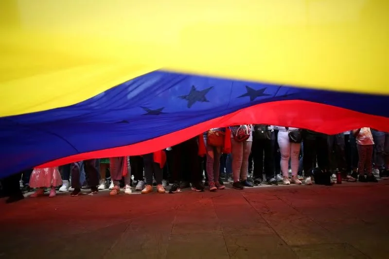 Una gran bandera de Venezuela ondeando en primer plano, cubriendo parcialmente a una multitud de personas. Imagen que representa la propuesta de doble nacionalidad de Gustavo Petro para ciudadanos venezolanos en Colombia.