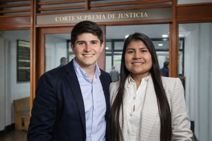 Los congresistas colombianos Wadith Manzur y Karen Manrique posan sonriendo frente a la entrada principal de la Corte Suprema de Justicia durante una diligencia relacionada con el escándalo de corrupción de la UNGRD.