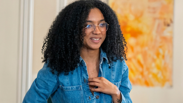 Una fotografía de Juliana Guerrero, exasesora capturada bajo cargos de fraude procesal relacionado con diplomas universitarios falsos (cartones chimbos). La imagen la muestra sentada en un café con una expresión pensativa y trenzas en el cabello, vistiendo una chaqueta negra y un collar de cruz. Esta fotografía se ha convertido en una imagen editorial clave tras su detención y su vinculación con las recientes declaraciones de Donald Trump sobre el 'infierno judicial' y el 'narcoterrorismo' en Venezuela y Colombia.