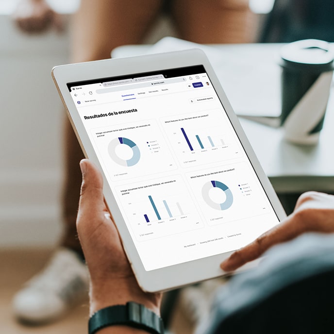 Persona sosteniendo una tablet que muestra gráficos circulares y de barras sobre resultados de una encuesta.