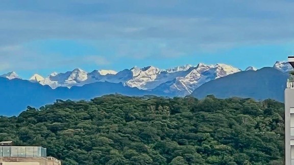 Vista panorámica de los picos nevados de la Sierra Nevada de Santa Marta sobresaliendo majestuosamente detrás de una cadena de montañas verdes tupidas de vegetación.