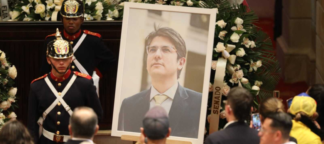 Fotografía de un funeral de Estado en el Congreso de Colombia. Se observa un gran retrato del político Miguel Uribe Turbay rodeado de coronas de flores blancas, custodiado por la Guardia Presidencial con uniforme de gala, mientras asistentes observan con respeto.
