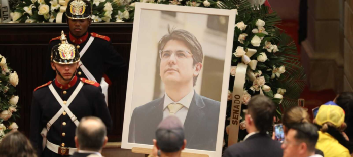 Fotografía de un funeral de Estado en el Congreso de Colombia. Se observa un gran retrato del político Miguel Uribe Turbay rodeado de coronas de flores blancas, custodiado por la Guardia Presidencial con uniforme de gala, mientras asistentes observan con respeto.