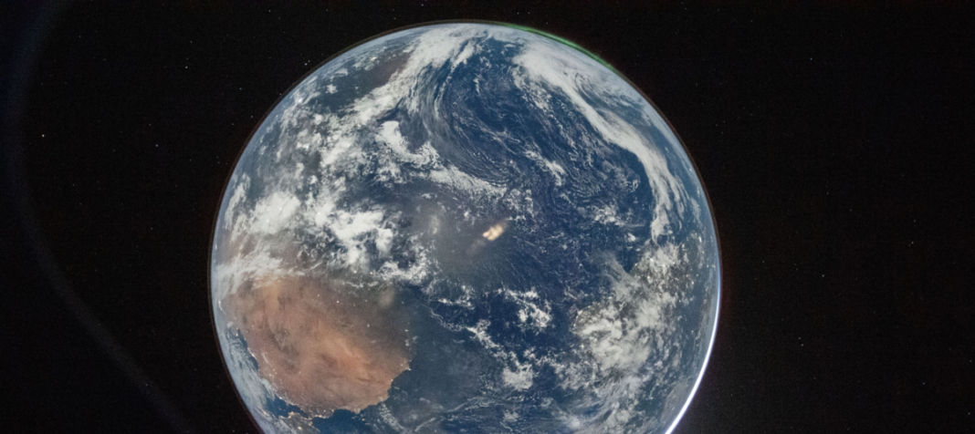 Vista completa de la Tierra desde el espacio profundo, mostrando el continente australiano y el Océano Pacífico, con una delgada capa atmosférica verde visible en el borde iluminado.