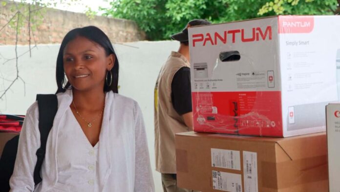 Una mujer sonríe junto a cajas de suministros y una impresora nueva durante la entrega de insumos de la Unidad para las Víctimas en Dibulla, La Guajira.