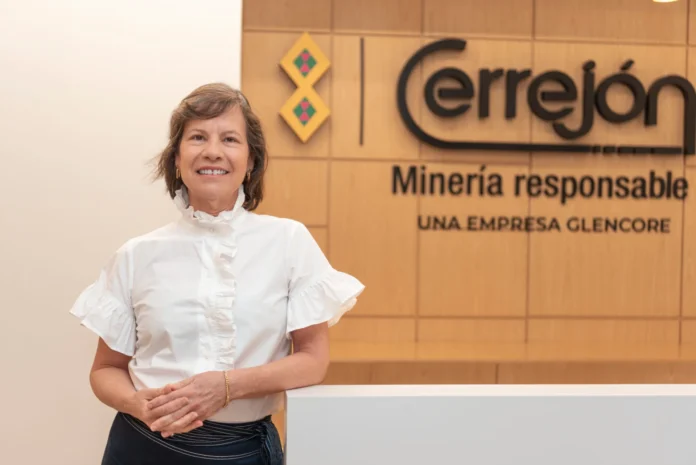 Claudia Bejarano, presidenta de Cerrejón, sonriendo con una blusa blanca elegante frente a un panel de madera con el logo de Cerrejón y el eslogan 