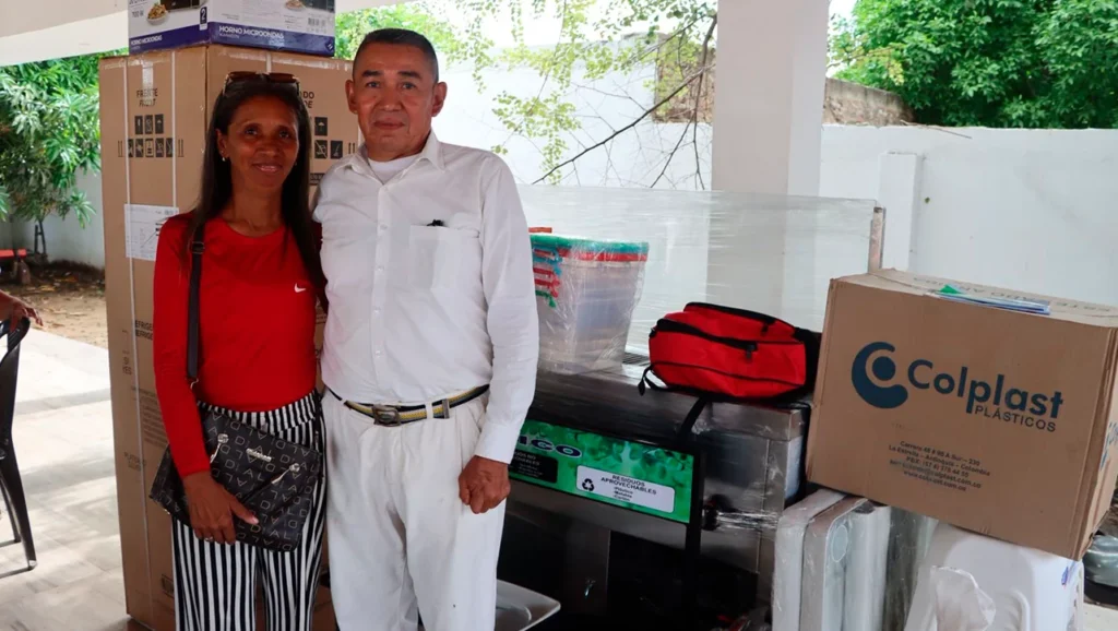 Una pareja de beneficiarios posa junto a neveras, cajas de suministros y maquinaria entregada por la Unidad para las Víctimas en Dibulla.