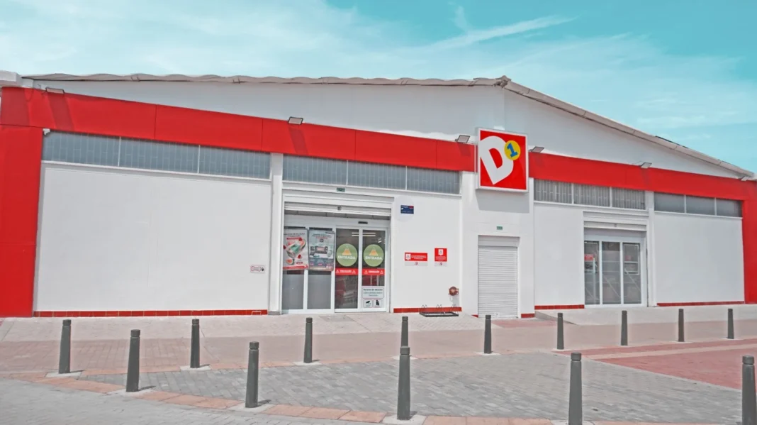 Fachada de una Tienda D1 en Colombia con su logotipo rojo y blanco, bajo un cielo azul con nubes, ilustrando la noticia sobre el pliego de cargos de la SIC.