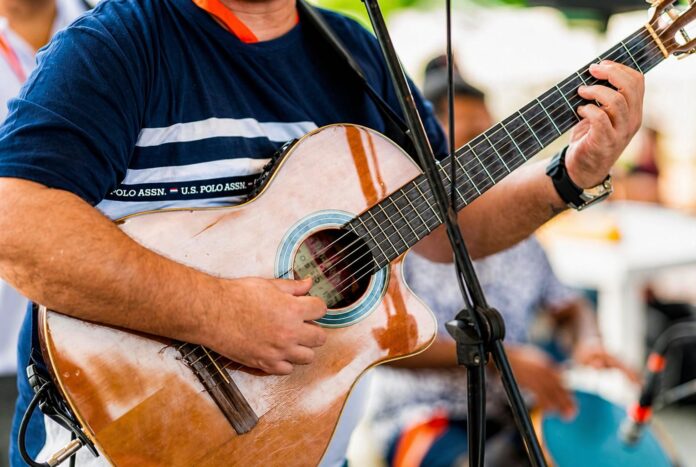 Primer plano de un músico tocando una guitarra acústica de madera en un evento al aire libre.