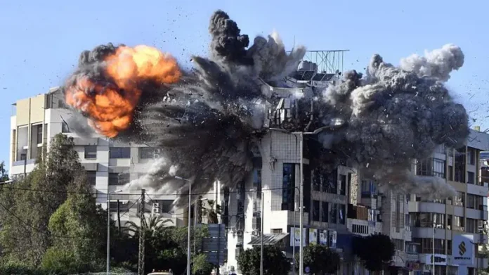 Momento exacto de una explosión masiva en un edificio residencial tras un ataque aéreo en el Líbano, con fuego, escombros volando y densas columnas de humo gris.