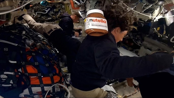 Un frasco de Nutella flota en gravedad cero dentro de la nave Orion durante la misión Artemis II de la NASA, mientras dos astronautas trabajan al fondo.