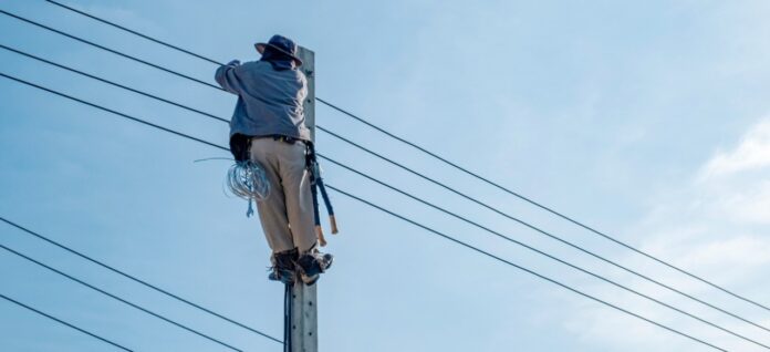 Un técnico electricista trepado en un poste de concreto manipulando las líneas de energía.