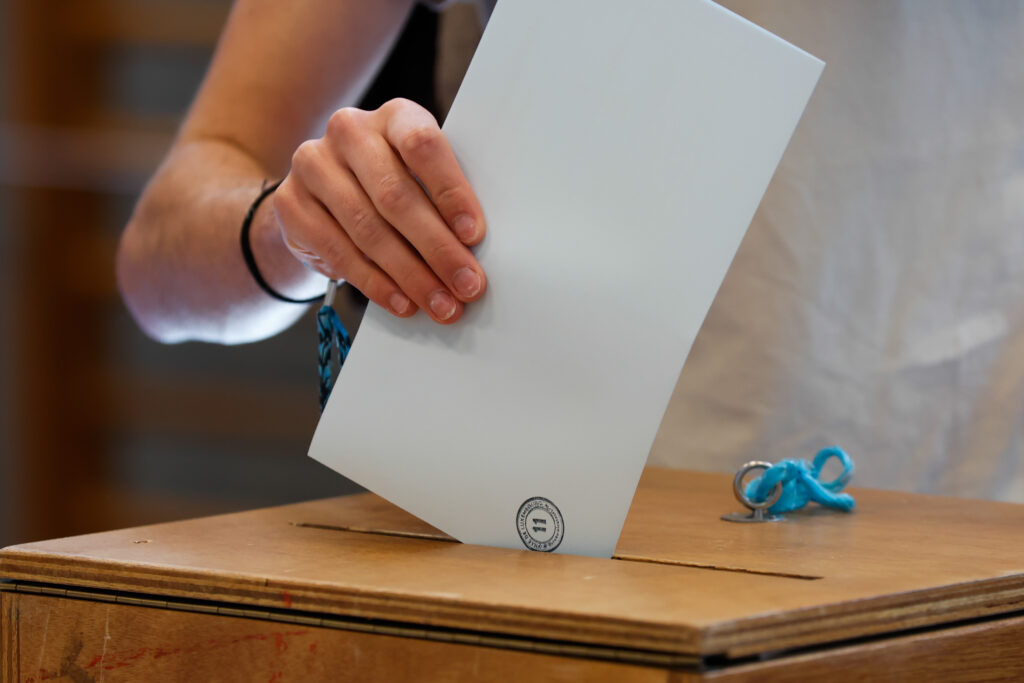 Primer plano de una persona depositando su voto en una urna de madera, como símbolo de transparencia en la investigación contra Invamer y otros procesos electorales.