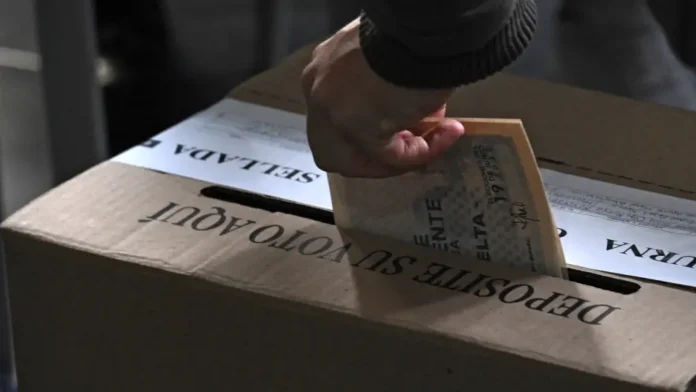 Primer plano de la mano de un votante depositando su tarjetón en una urna de cartón durante una jornada electoral en Colombia.