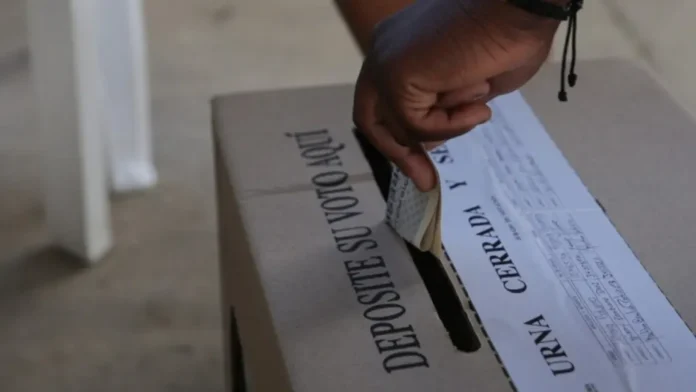 Elecciones presidenciales 41 millones habilitados: Fotografía de primer plano donde la mano de un ciudadano deposita su tarjetón electoral doblado dentro de una urna de cartón.