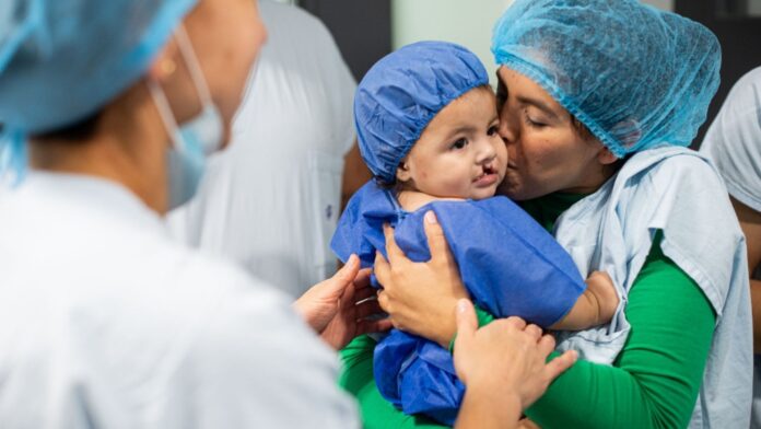 Una madre abraza y besa a su bebé con labio fisurado mientras el equipo médico de Operación Sonrisa en Valledupar asiste la escena