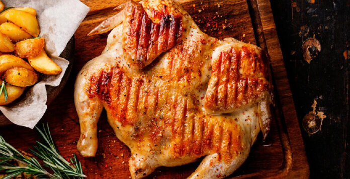 Precio del pollo asado: Fotografía en plano cenital de un pollo entero a la parrilla sobre una tabla de madera.