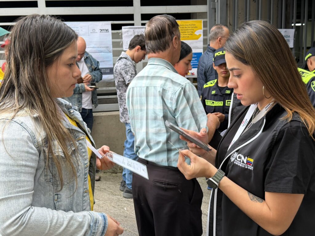 Funcionaria del Consejo Nacional Electoral (CNE) revisando la escarapela y datos de una testigo electoral en la entrada de un puesto de votación.