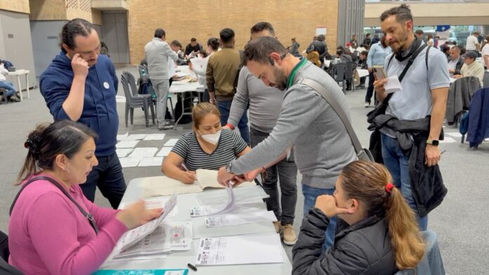 Mesa de votación y ciudadanos colombianos realizando trámites de verificación e inscripción de actas electorales.