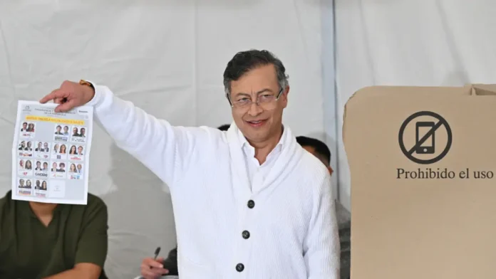 Petro campaña Iván Cepeda segunda vuelta: El presidente Gustavo Petro sonríe mientras muestra el tarjetón electoral oficial frente a un cubículo de votación.