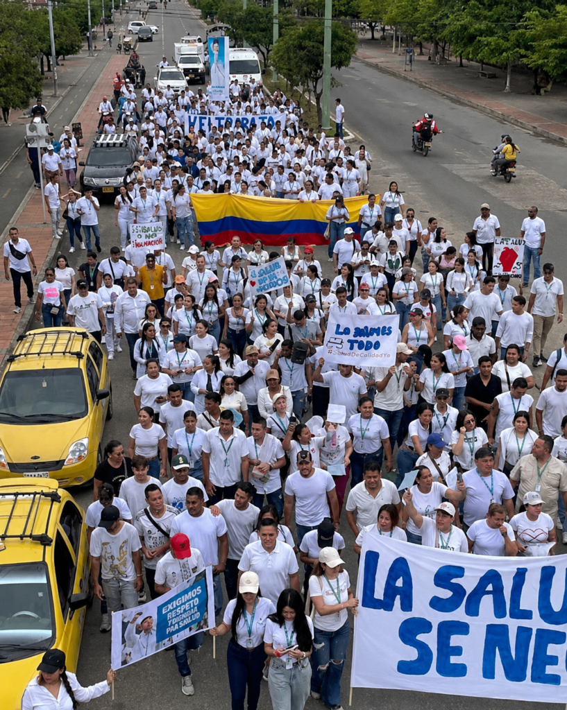 Ciudadanos marchan vestidos de blanco con pancartas y una bandera de Colombia para exigir respeto, dignidad y mejores servicios de salud.
