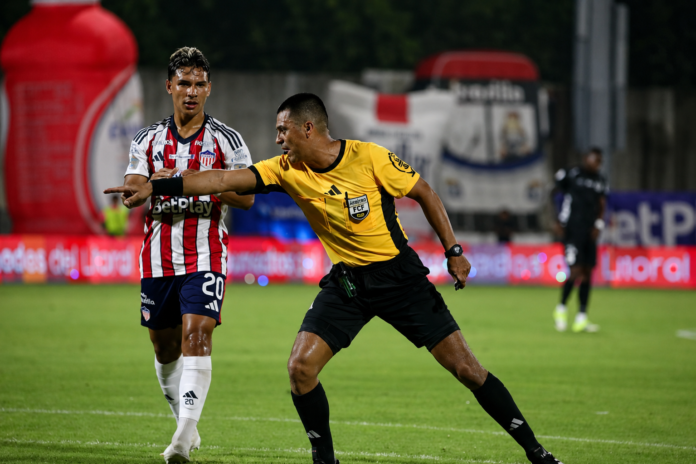 Árbitro señala una decisión durante un partido del fútbol profesional colombiano.