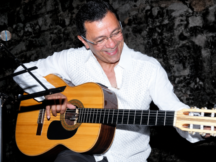 Fernando Meneses sonríe mientras sostiene una guitarra durante una presentación musical
