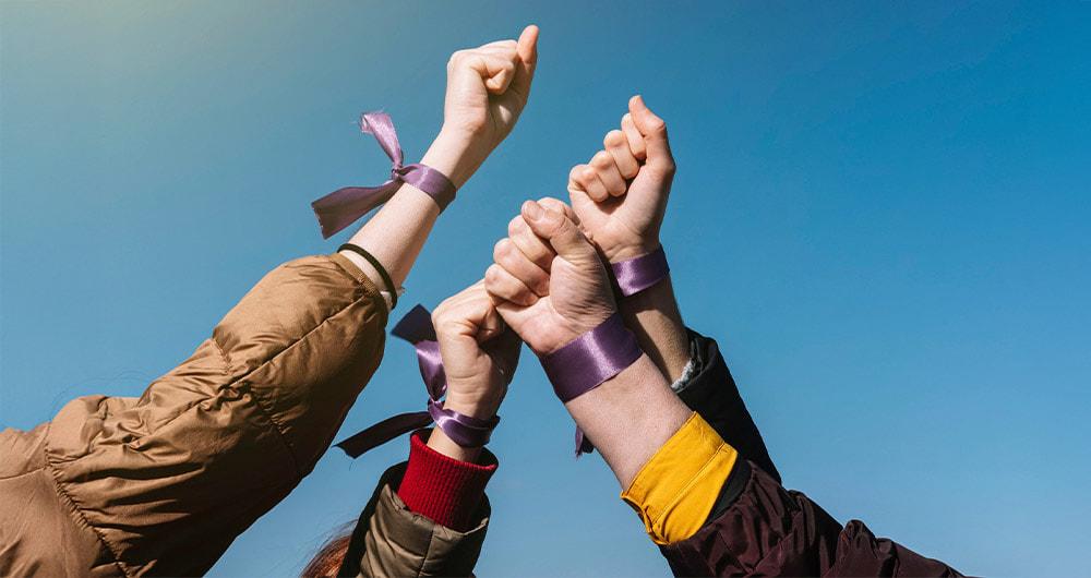 Mujeres levantan sus manos con cintas moradas como símbolo de rechazo a la violencia de género