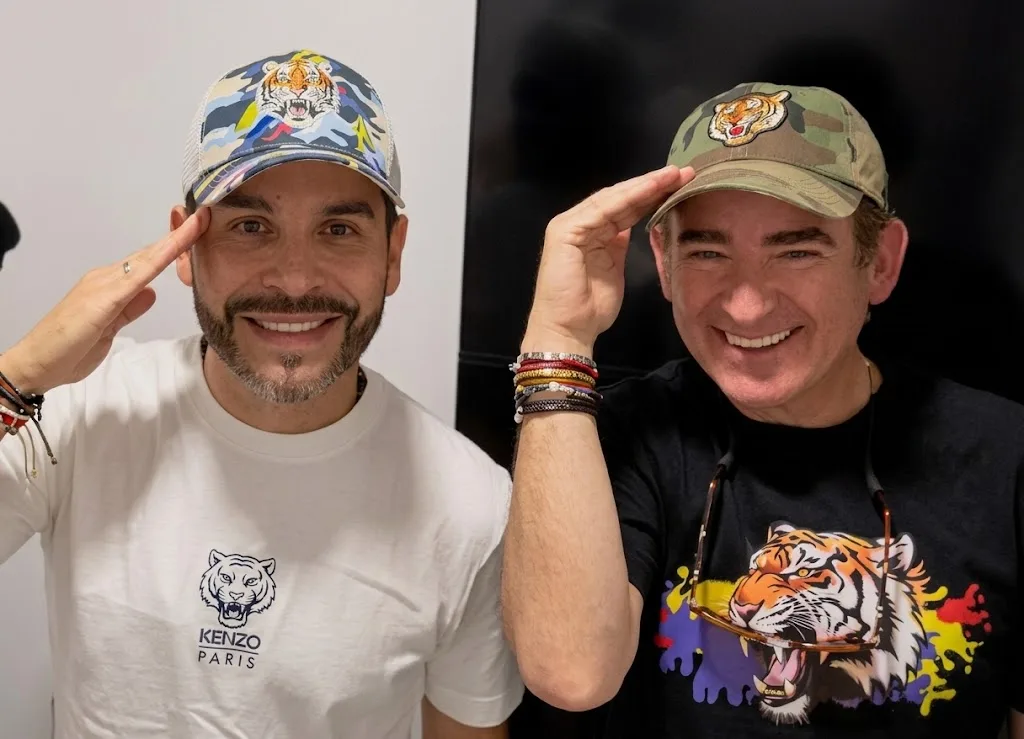 Dos hombres posan juntos usando gorras y camisetas con diseños de tigres