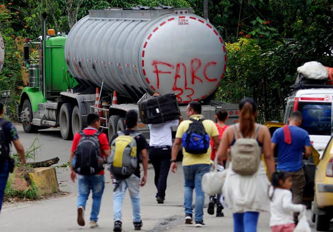 Habitantes transitan por una vía rural junto a un vehículo con grafitis alusivos a las FARC, en una zona afectada por el conflicto armado en Colombia.
