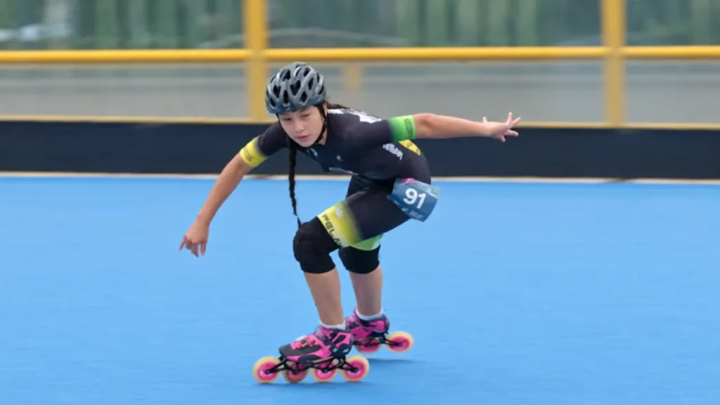 Patinadora con casco, rodilleras y dorsal 91 durante su recorrido por una pista azul.