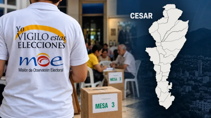 Observador electoral con camiseta de la MOE junto a un puesto de votación y un mapa del departamento del Cesar.