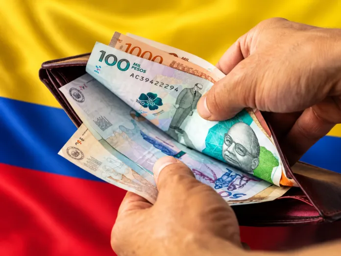 Billetes colombianos en una billetera con la bandera de Colombia difuminada, imagen alusiva al salario mínimo en Colombia.