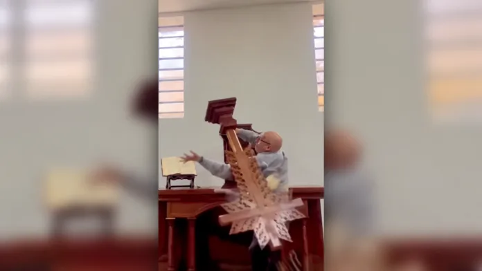 Caída de una cruz sobre un hombre que intenta manipular una estructura religiosa dentro de una iglesia.