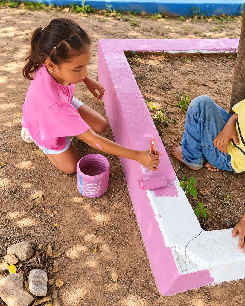 Niña participa en la recuperación del parque de La Junta pintando de rosado una jardinera.