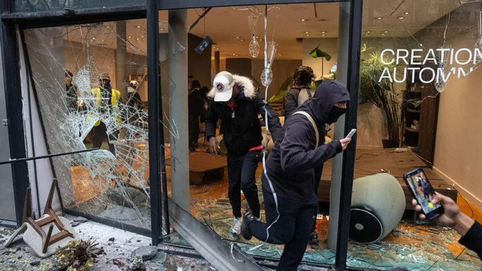 Personas salen de una tienda con la vitrina rota durante saqueos registrados en París, en medio de los disturbios de octubre de 2026.